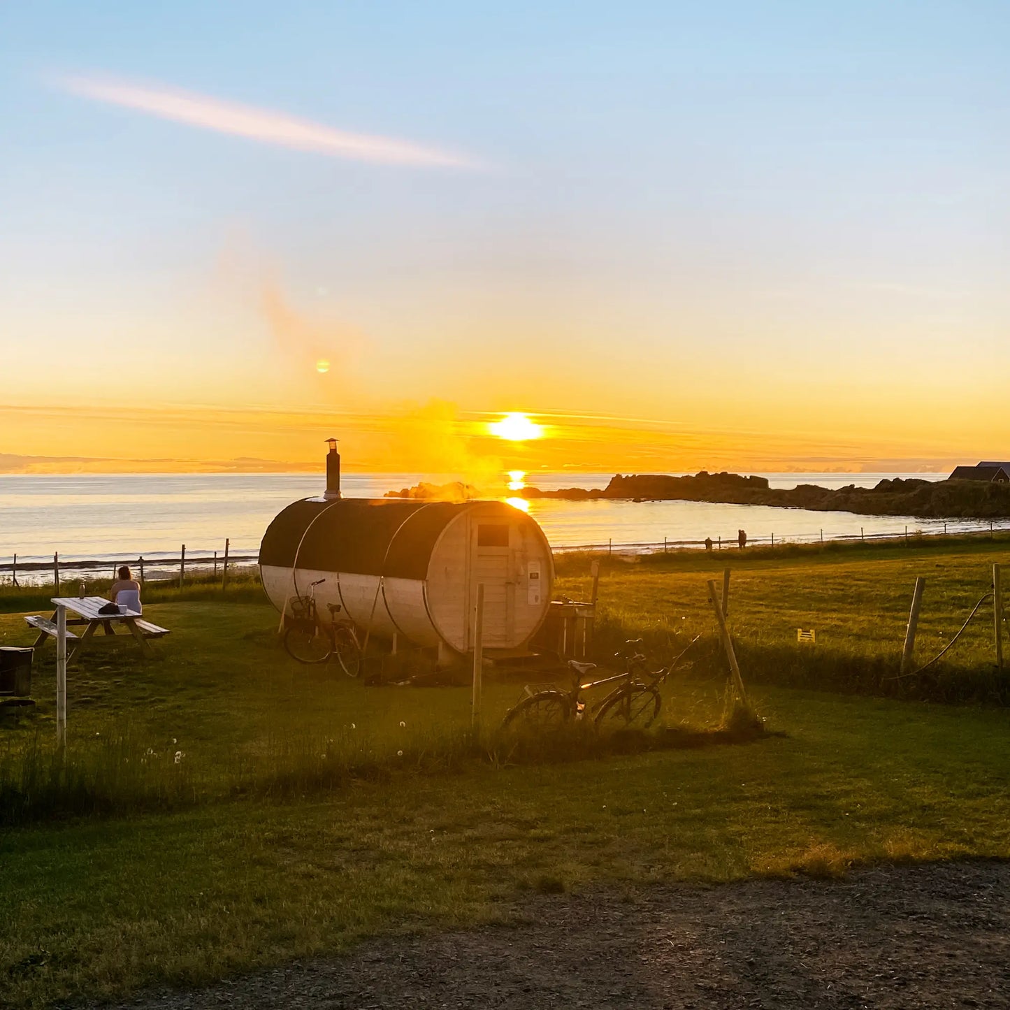 Sauna in Lofoten. Backdrop is an orange midnight sun and green grass.