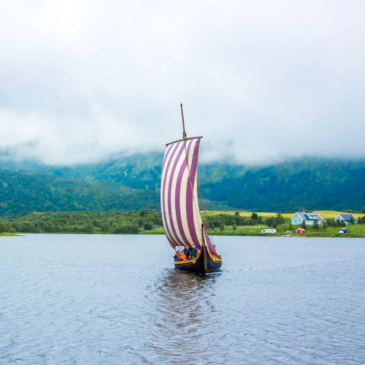 Traditional Viking ship with red and white striped sail in Borge, Lofoten. The water is blue and there is fog around.